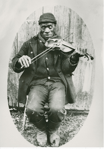 A black and white photography of an African man in a winter coat and hat, playing a fiddle.