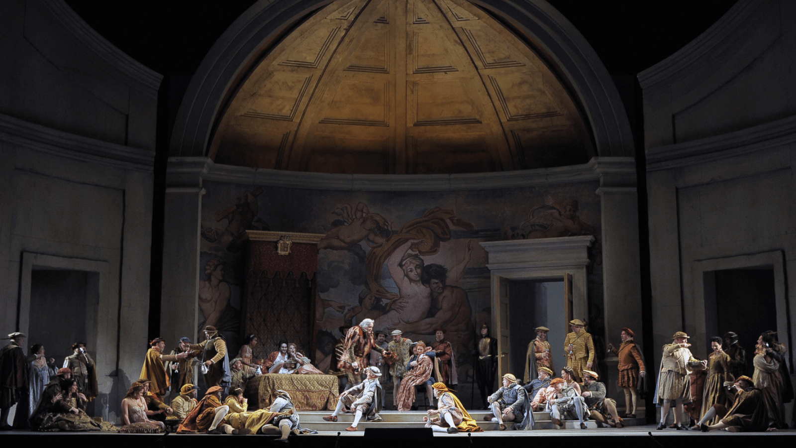 A large crowd in Renaissance attire, standing and sitting in various positions around the stage. 