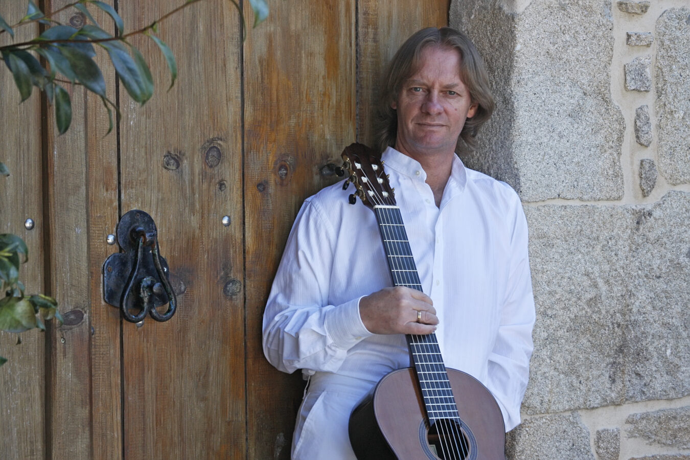 David Russel posing with a guitar in front of a wooden door