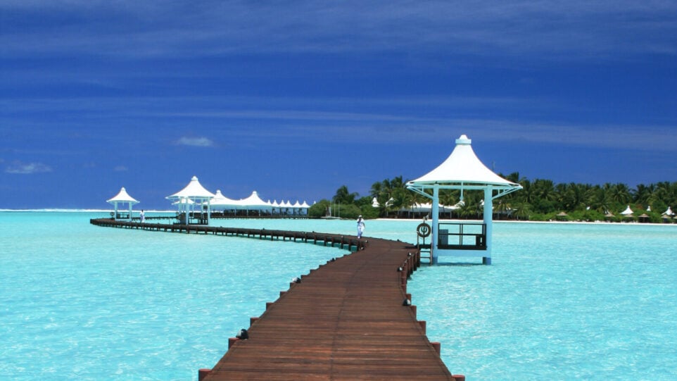 tropical scene with boardwalk and shacks over aquamarine ocean water
