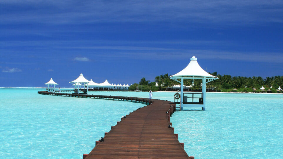 tropical scene with boardwalk and shacks over aquamarine ocean water