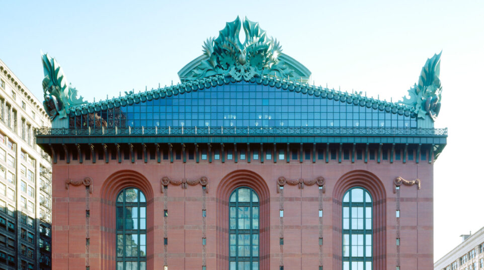 A straight-on shot of the Chicago Public Library's Harold Washington Library, a tall stout brick building with a glass and mint-copper top