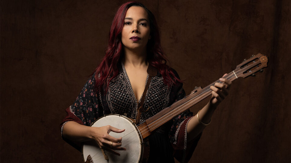 Rhiannon Giddens stares solemnly while playing a banjo