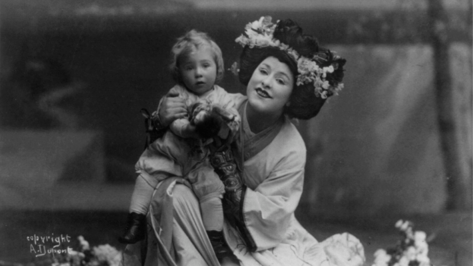 Black and white image of Geraldine Farrar, kneeling child on knee, facing slightly left, in Madame Butterfly.