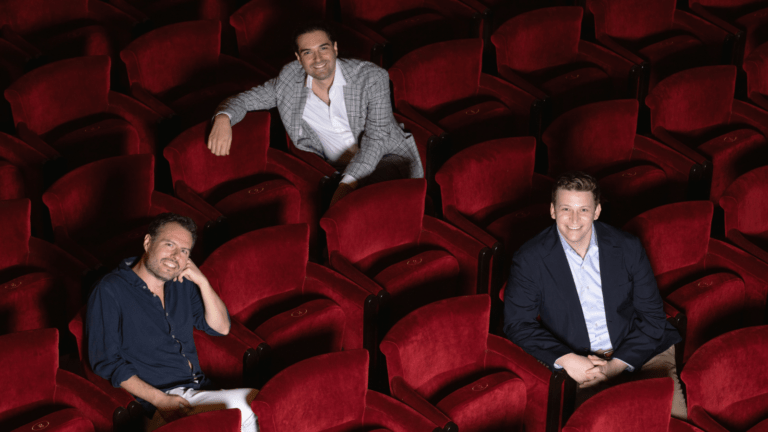 Raffaele Pe, Carlo Vistoli and Aryeh Nussbaum Cohen seated on the red upholstered seats of the auditorium of Teatro dell'Opera di Roma; smiling in business casual attire.