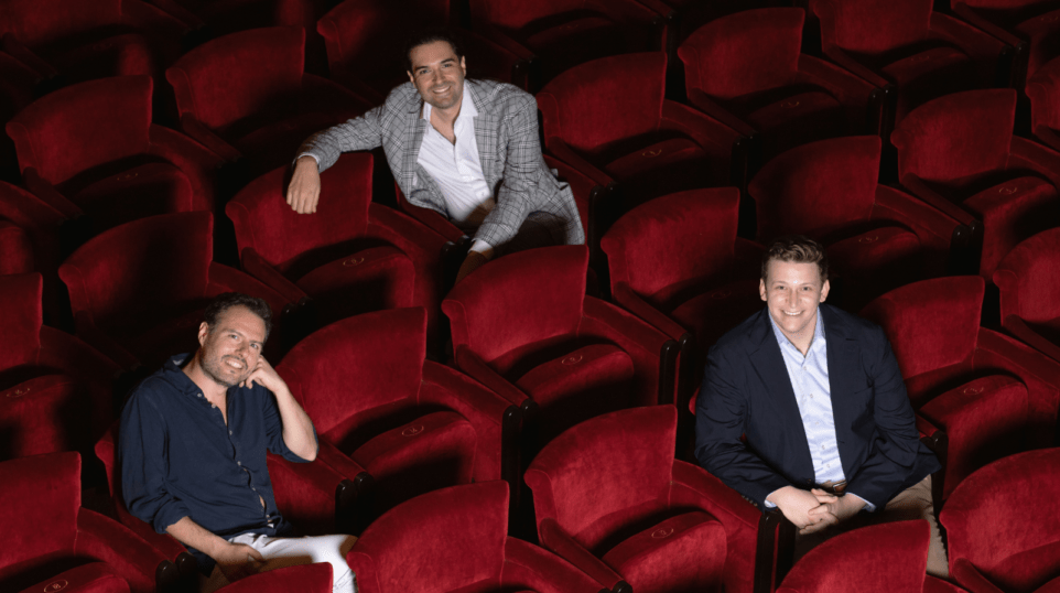 Raffaele Pe, Carlo Vistoli and Aryeh Nussbaum Cohen seated on the red upholstered seats of the auditorium of Teatro dell'Opera di Roma; smiling in business casual attire.