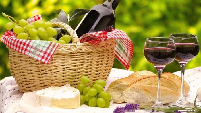 a picnic basket with a bottle of wine, two glasses, cheese and grapes