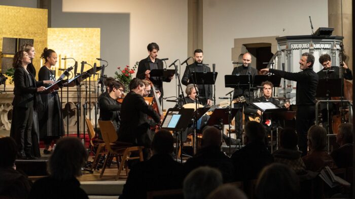 A group of musicians playing stringed instruments of the Renaissance and 3 famle and 3 male singers and a conductor perform in a church