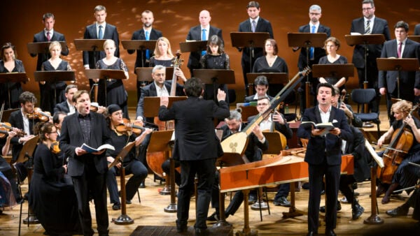 Zelenka's Missa Omnium Sanctorum Two male singers front an early music ensemble and a row of women singers and a row of male singers. A conductor faces the ensemble.
