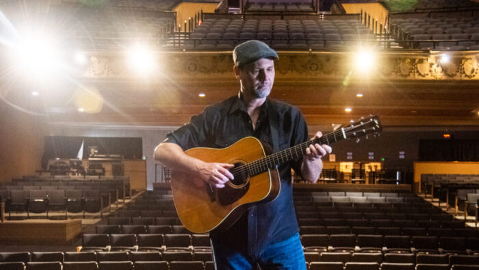 man stands with guitar in empty theatre