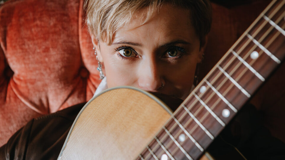 blonde woman peers over her guitar