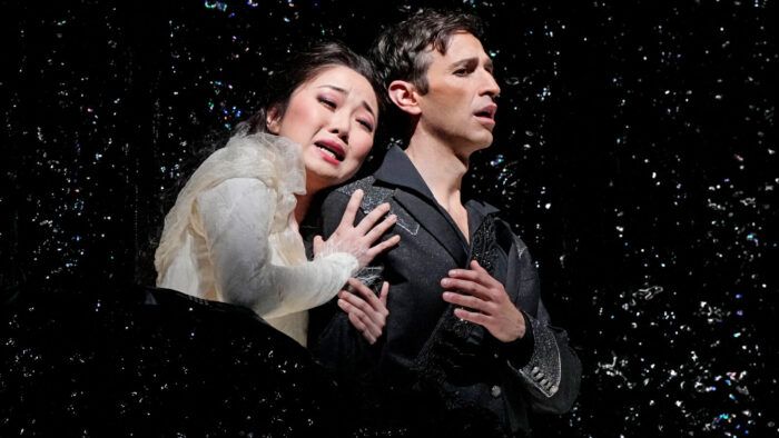 A woman sorrowfully embraces a man, who mournfully looks away