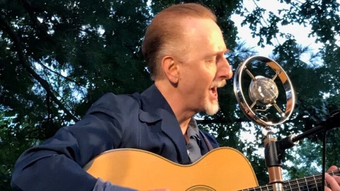 man with guitar sings into old style microphone