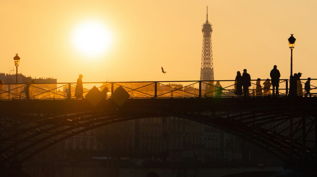 A goldent sunset with Eiffel tower in the background and pedestrians on a bridge in the forground