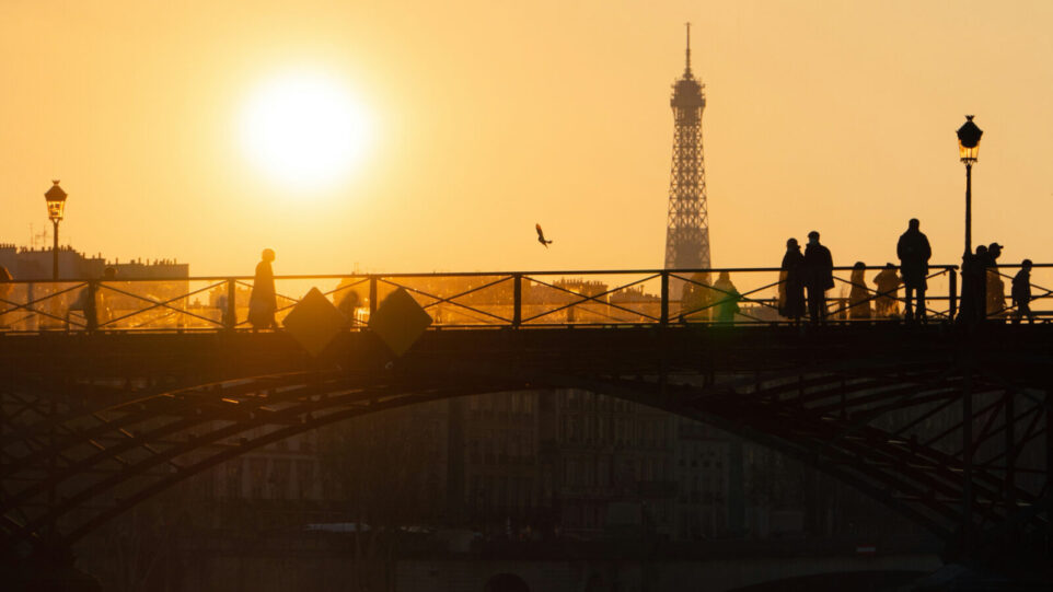 A goldent sunset with Eiffel tower in the background and pedestrians on a bridge in the forground