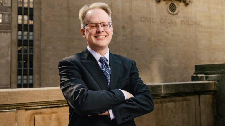 Man in suit and dotted necktie smiles in front of the Civic Opera Building