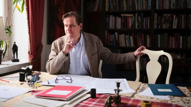 Mustonen gazes thoughtfully at the camera in a study filled with books and papers