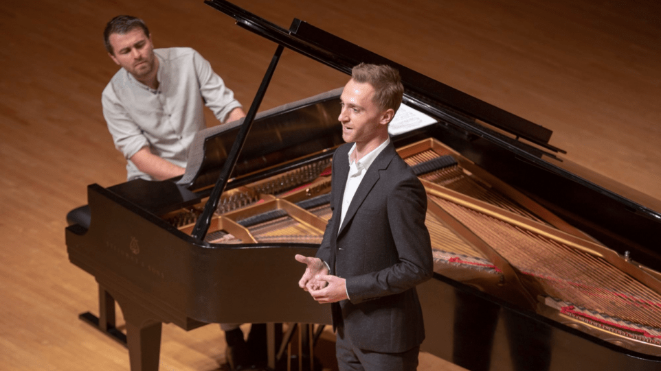 Bariotne Dominik Belavy standing in the crook of Steinway grand piano, wearing a dark suit, light shirt, no tie; pianist Daniel Gerzenberg at the keyboard, in shirt sleeves, rolled to elbow.