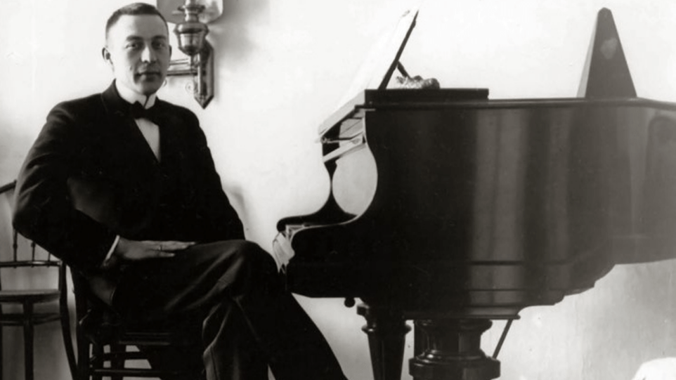 A young Rachmaninoff sits at the piano, black and white photo.