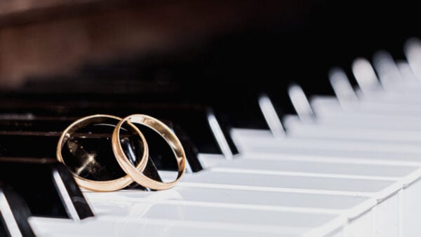 a pair of gold wedding bands rest together on the keys of a piano