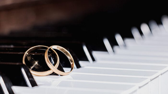 a pair of gold wedding bands rest together on the keys of a piano
