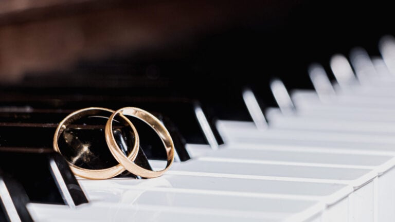a pair of gold wedding bands rest together on the keys of a piano