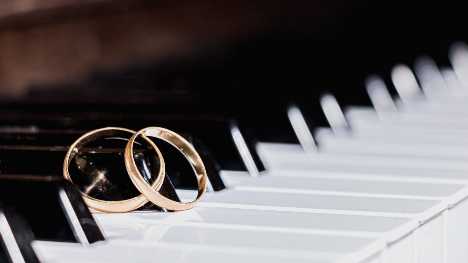 a pair of gold wedding bands rest together on the keys of a piano