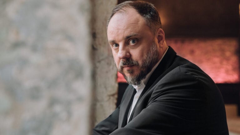 Portrait of Matthias Goerne in dark suit, light shirt, looking over his left shoulder