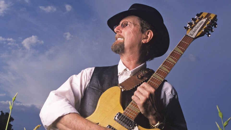 smiling man holds guitar and looks up at the sky