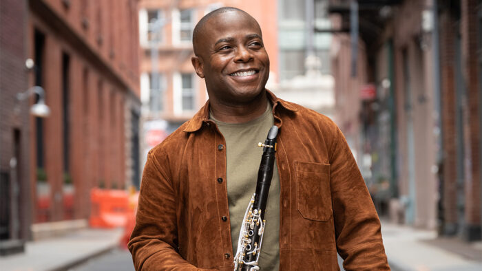 Man in shirt and suede overshirt smiles holding clarinet