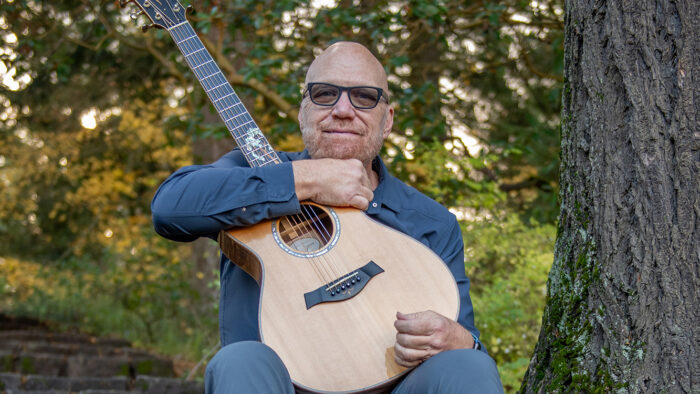 man with guitar on stone steps next to a tree