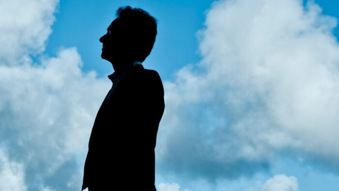 Shai Wosner framed in silhouette against a vibrant blue cloudy sky