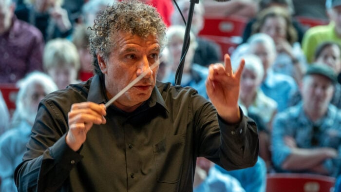 Man conducts animatedly with audience in backgroudn