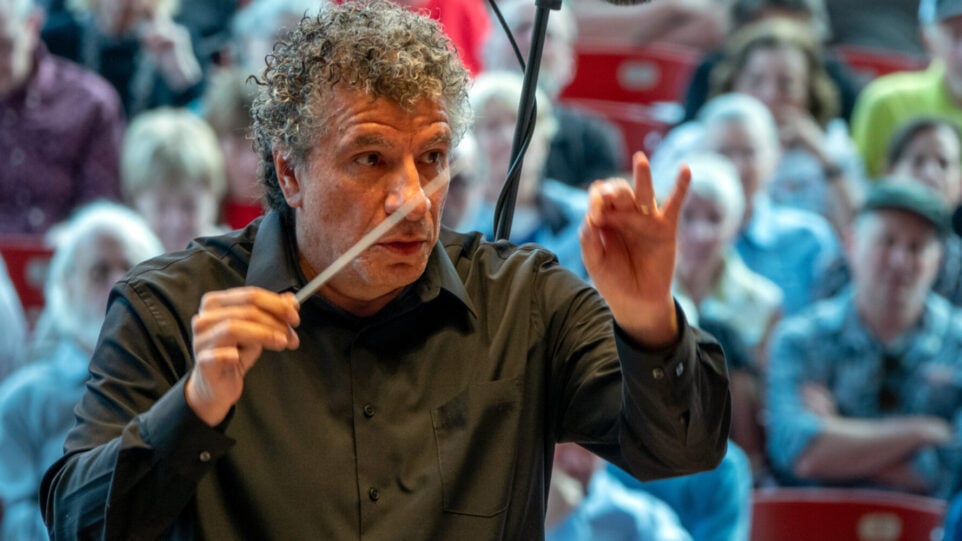 Man conducts animatedly with audience in backgroudn