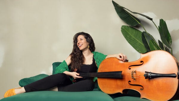 Cellist and composer Andrea Casarrubios poses on green couch with her cello