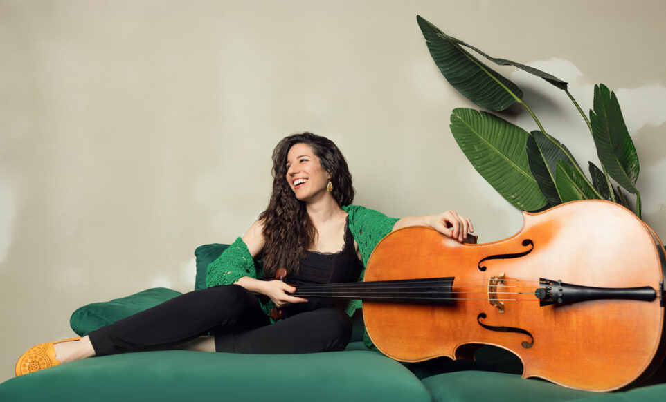Cellist and composer Andrea Casarrubios poses on green couch with her cello
