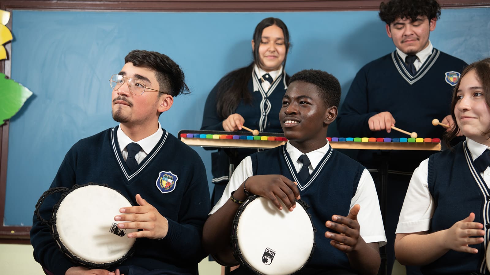 Students in school uniforms playing xylophones and djembe drums.