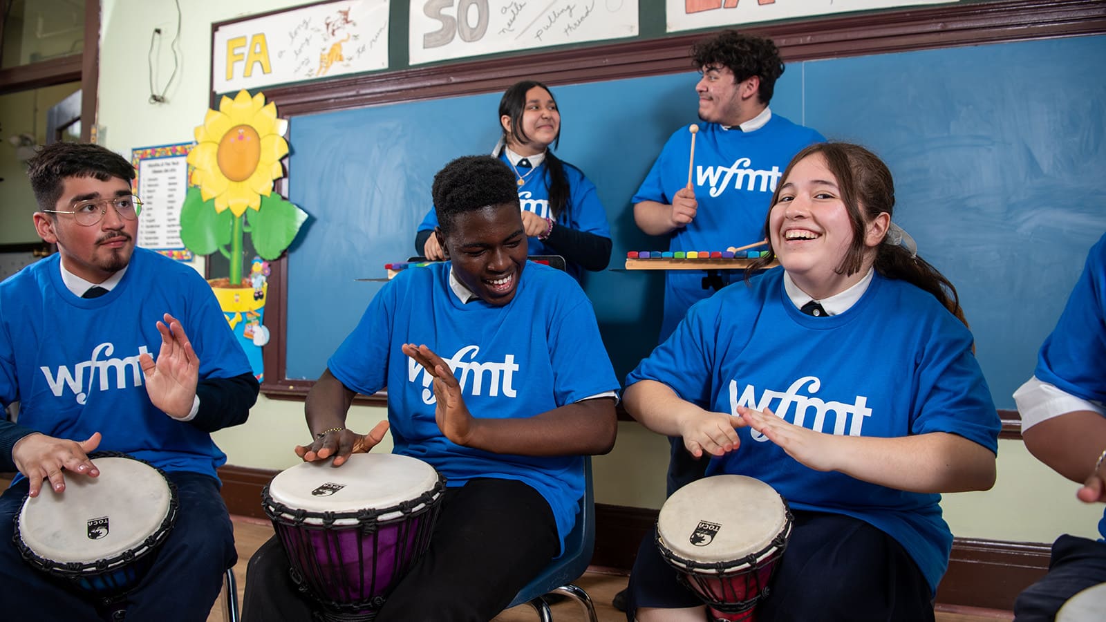 Students in blue WFMT t-shirts playing a variety of musical instruments
