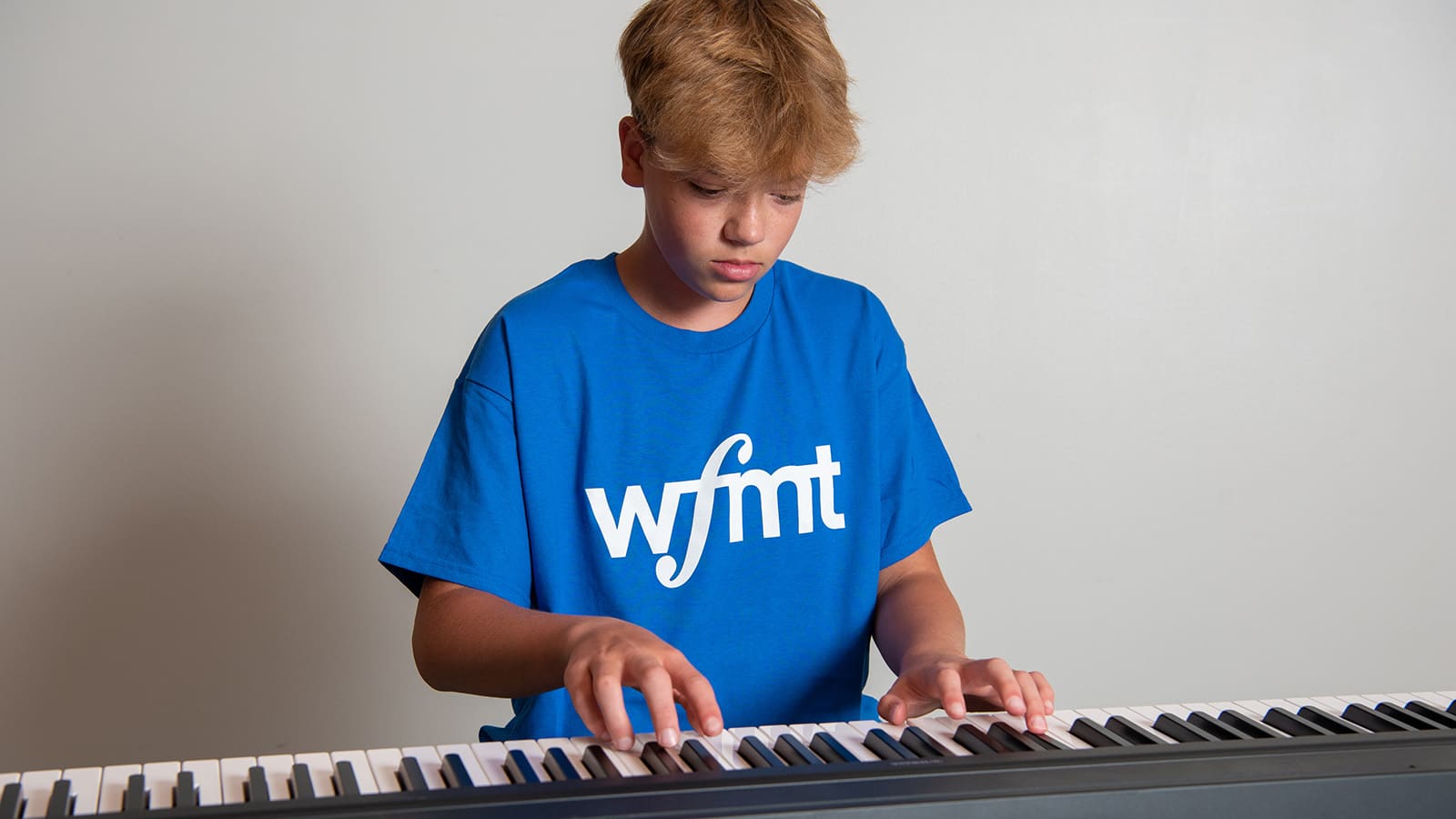 Student in a blue WFMT t-shirt playing a keyboard