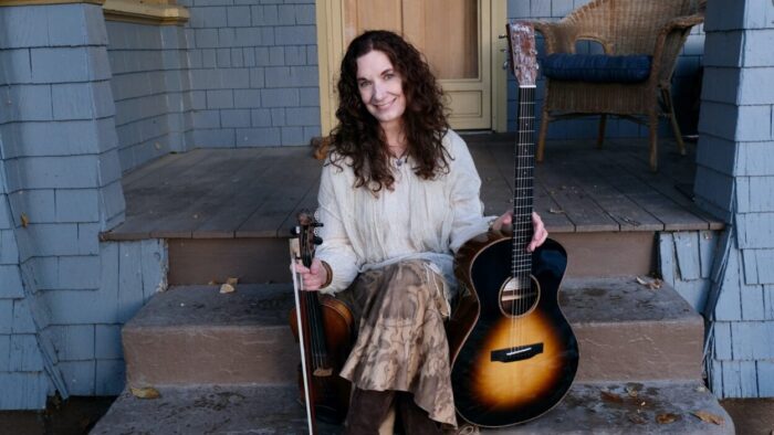 woman on porch steps holding guitar and fiddle