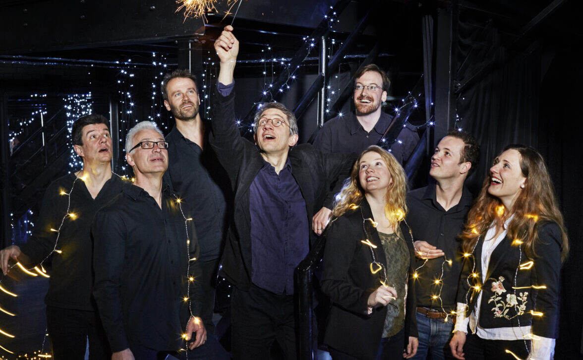 8 happy people adorned with lights on strings, on with a sparkler above his head