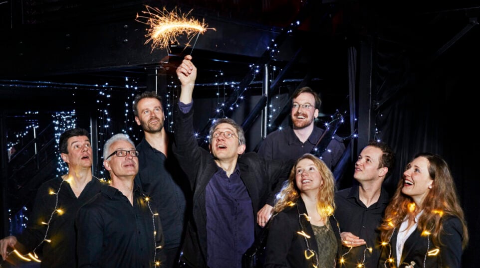 8 happy people adorned with lights on strings, on with a sparkler above his head