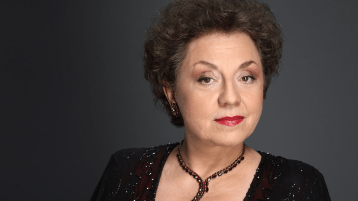 Portrait of Ewa Podleś in a beaded black dress and a dark beaded necklace facing the forward, dark background.