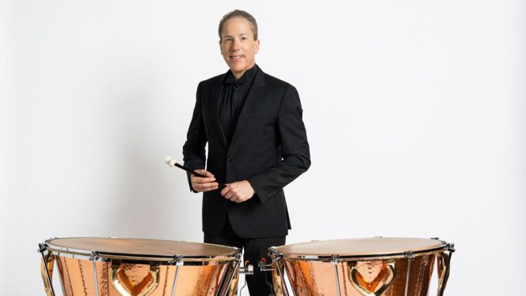 Man in dark suit poses with timpani