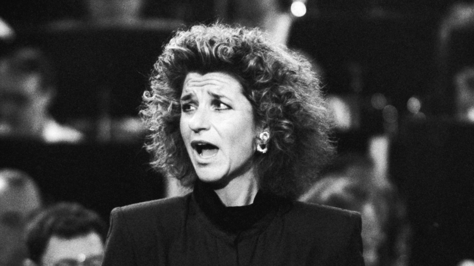 Black and white image of Agnes Baltsa in concert, jaw dropped and looking over right shoulder, wearing a dark suit.