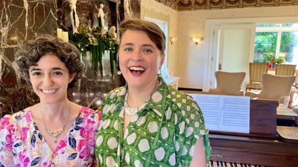 two smiling women infront of a piano