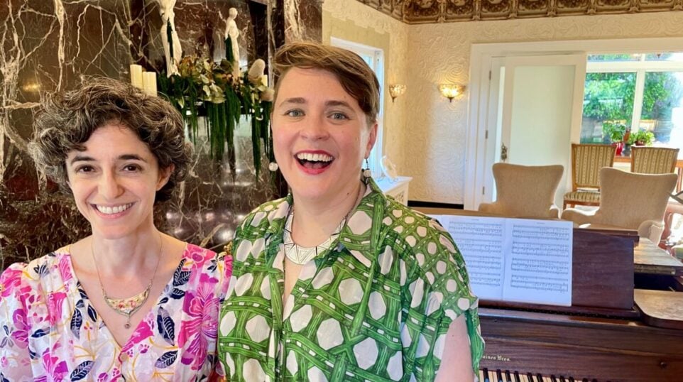two smiling women infront of a piano