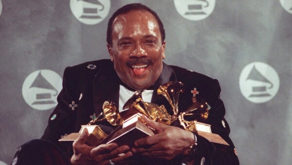 Quincy Jones grins while holding multiple Grammy Awards