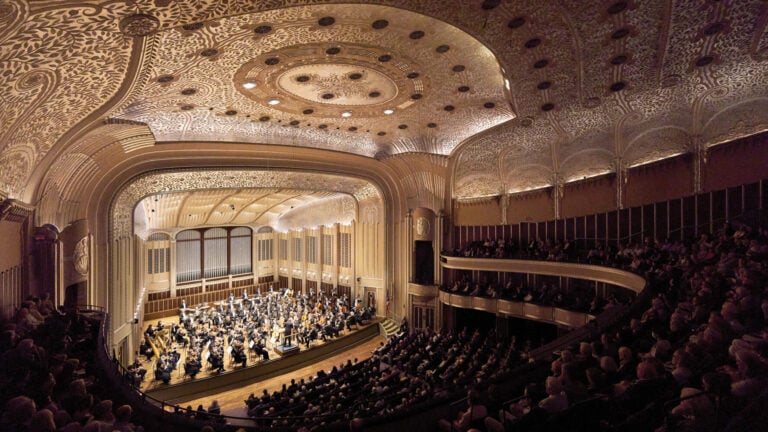 Richly adorned concert hall with full orchestra and audience
