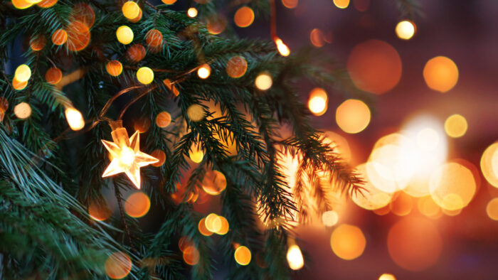 Closeup of glimmering Christmas tree with an illuminated star and golden background lights